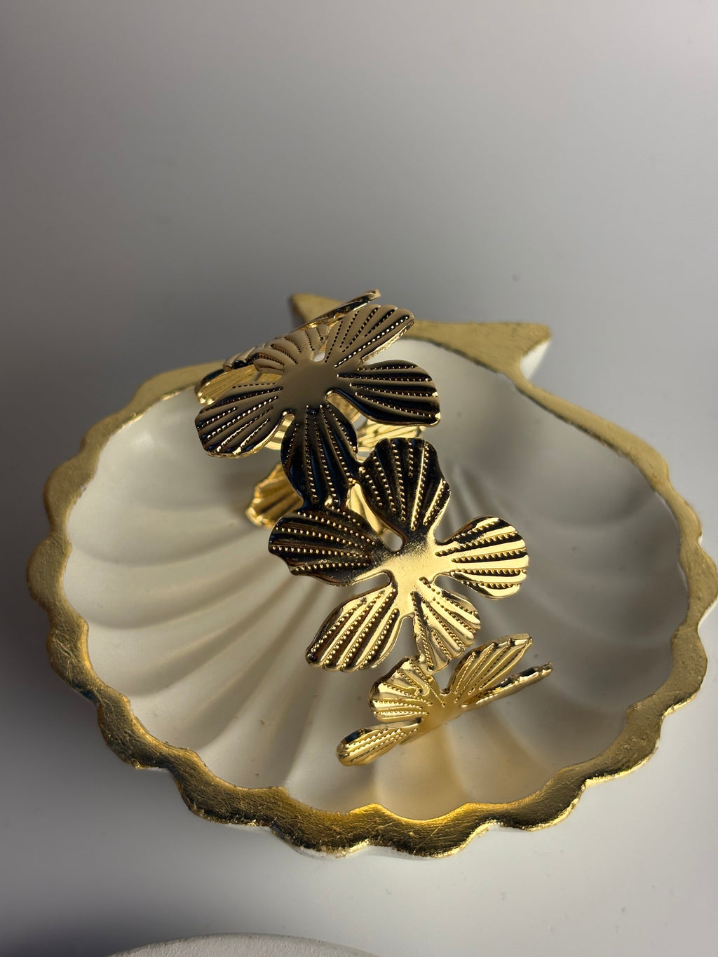 Three gold-tone butterfly-shaped earrings with textured, ribbed details displayed inside a white scalloped shell-shaped dish on a neutral gray background.