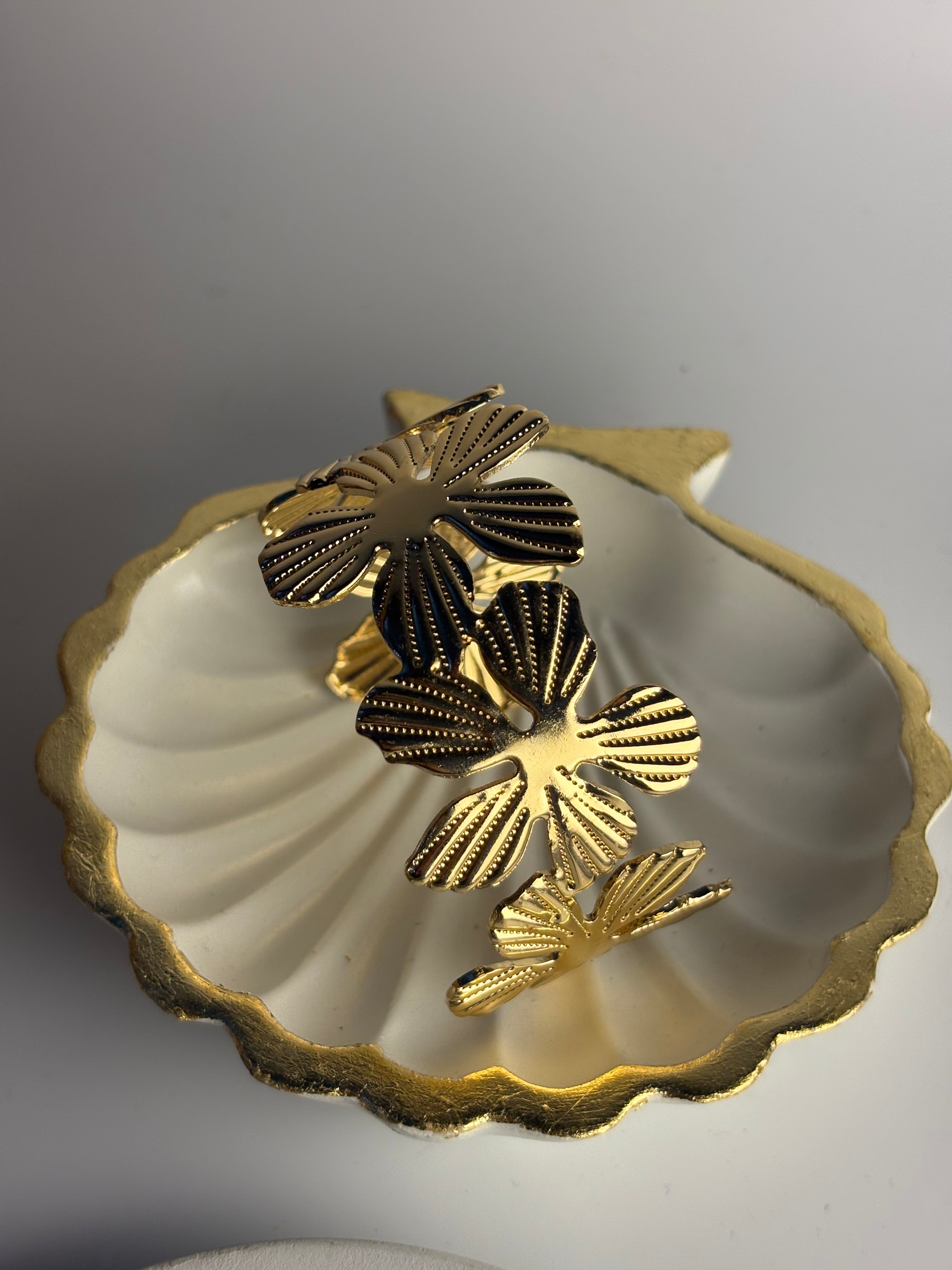 Three gold-tone butterfly-shaped earrings with textured, ribbed details displayed inside a white scalloped shell-shaped dish on a neutral gray background.